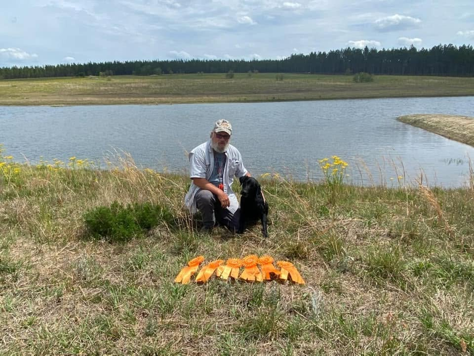 Clay Hasty with a dog, ribbons, and pond at field trial grounds