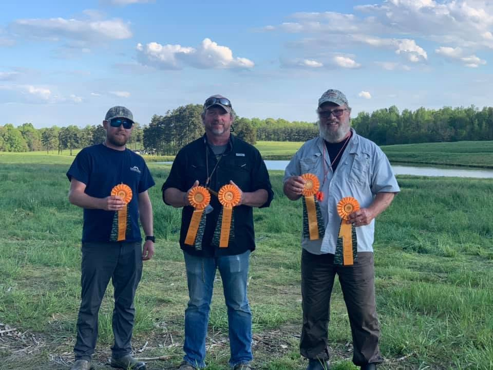 Handlers holding orange field trial ribbons near pond and field grounds